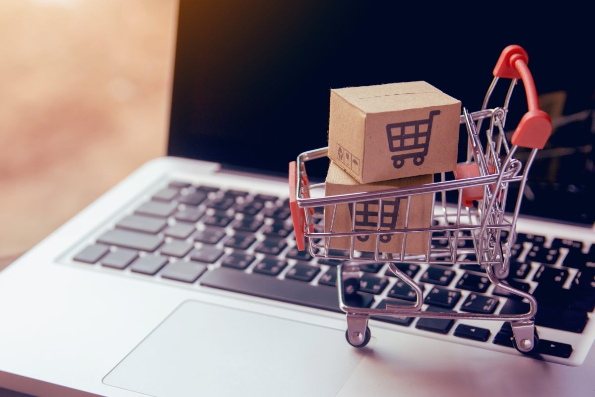 Dettaglio di un pc portatile aperto con un piccolo carrello con pacchetti di integratori alimentari acquistati online