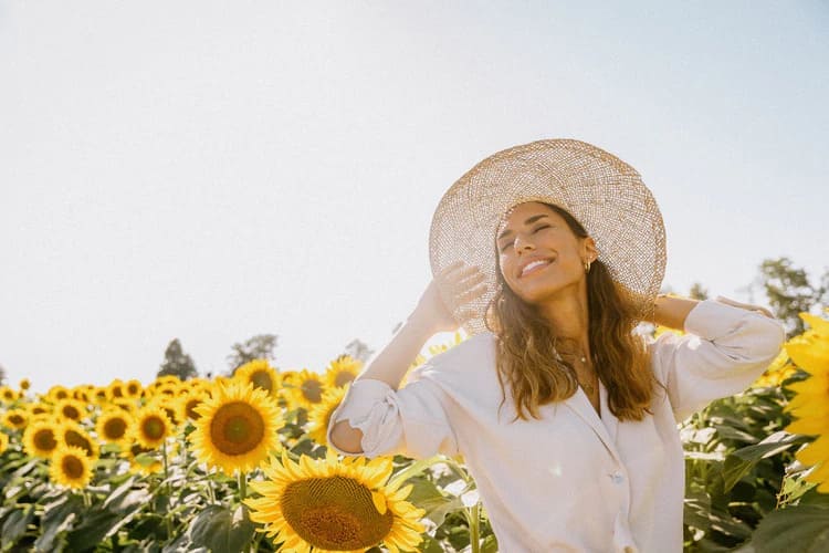 donna felice in un campo di girasoli in estate, sorride con un grande cappello in una giornata soleggiata al tramonto metagenics