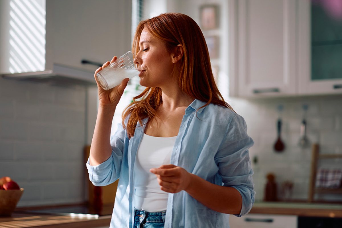 Donna in cucina beve un bicchiere d'acqua con Probactiol Fibre