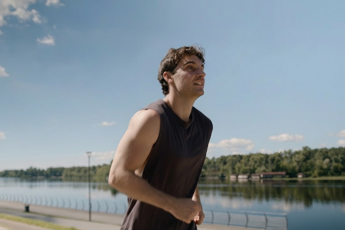 ragazzo corre su un marciapiede a bordo di un fiume alla luce del sole